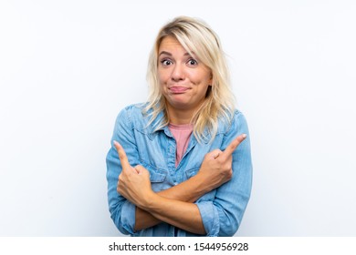 Young blonde woman over isolated white background pointing to the laterals having doubts - Shutterstock ID 1544956928