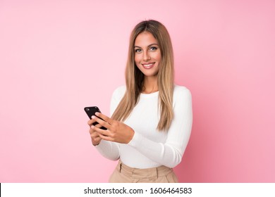 Young Blonde Woman Over Isolated Pink Background Sending A Message Or Email With The Mobile