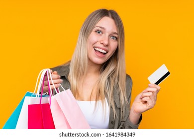 Young blonde woman over isolated yellow background holding shopping bags and a credit card - Shutterstock ID 1641984349
