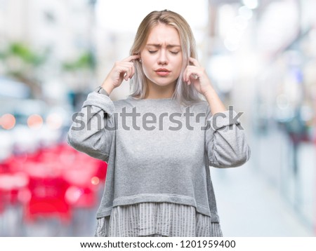 Young blonde woman over isolated background covering ears with fingers with annoyed expression for the noise of loud music. Deaf concept.