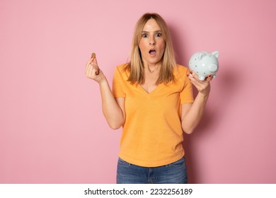 Young blonde woman over pink background holding piggy bank with a surprise face. - Shutterstock ID 2232256189