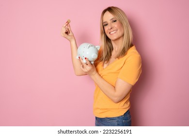 Young blonde woman over pink background holding piggy bank with a happy face standing and smiling with a confident smile showing teeth - Shutterstock ID 2232256191