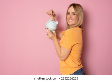 Young blonde woman over pink background holding piggy bank with a happy face standing and smiling with a confident smile showing teeth - Shutterstock ID 2232256235