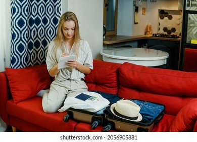 Young blonde woman packing suitcase making list of clothes and accessories going to summer travel vacation. Solo trip concept.