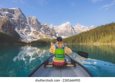 A young blonde woman paddles a canoe on the scenic, picturesque glacial Moraine Lake, a popular outdoor tourist destination in Banff National Park, Alberta, Canada in the Rocky Mountains.
