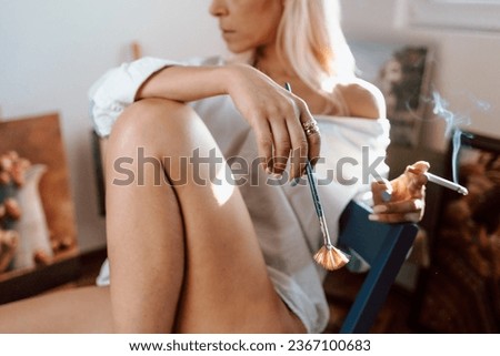Young, blonde woman painting and smoking a cigarette
