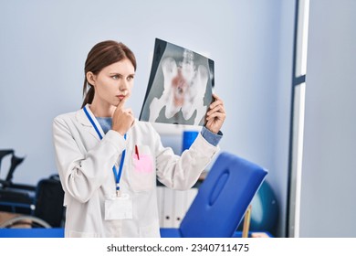 Young blonde woman physiotherapist looking xray thinking at rehab clinic