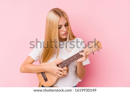 Young blonde woman playing ukelele isolated in a background