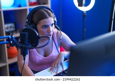 Young Blonde Woman Playing Video Games Talking With Microphone With The Audience Scared And Amazed With Open Mouth For Surprise, Disbelief Face 