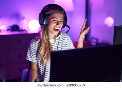 Young blonde woman playing video games smiling happy pointing with hand and finger to the side  - Powered by Shutterstock