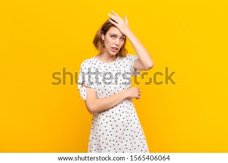 young blonde woman raising palm to forehead thinking oops, after making a stupid mistake or remembering, feeling dumb against flat color wall