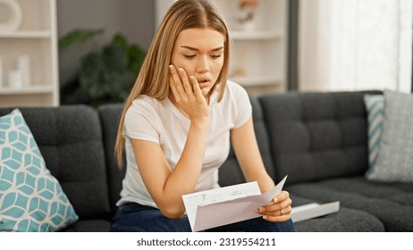 Young blonde woman reading letter sitting on sofa with worried expression at home - Powered by Shutterstock