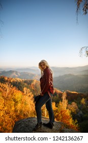 Young blonde woman in red jacket on top of the mountain. Happy traveler standing on top of a mountain and enjoying sunset view. Female stay on the top of mountain under sunlight - Shutterstock ID 1242136267