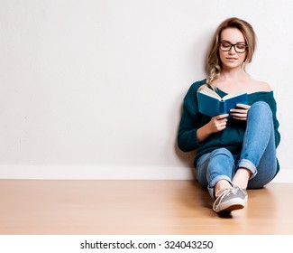 Young blonde woman relaxing on floor at home reading book. 