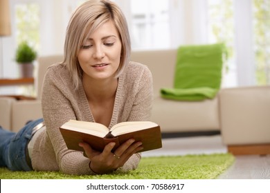 Young Blonde Woman Relaxing On Floor At Home Reading Book. Copyspace On Right.?