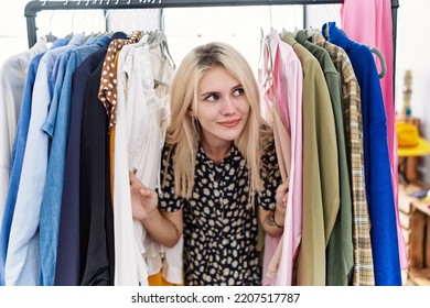 Young Blonde Woman Searching Clothes On Clothing Rack Smiling Looking To The Side And Staring Away Thinking. 