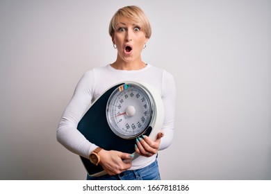 Young blonde woman with short hair holding scale for healthy weight and lifestyle scared in shock with a surprise face, afraid and excited with fear expression