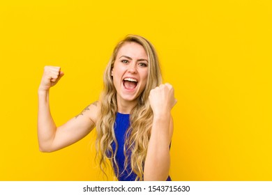 young blonde woman shouting triumphantly, looking like excited, happy and surprised winner, celebrating against yellow wall - Shutterstock ID 1543715630