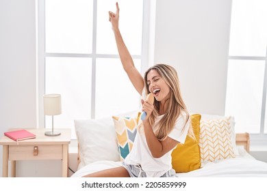 Young Blonde Woman Singing Song Using Brush As A Microphone At Bedroom