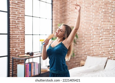 Young Blonde Woman Singing Song Using Brush As A Microphone At Bedroom