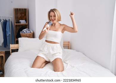 Young Blonde Woman Singing Song Using Brush As A Microphone At Bedroom