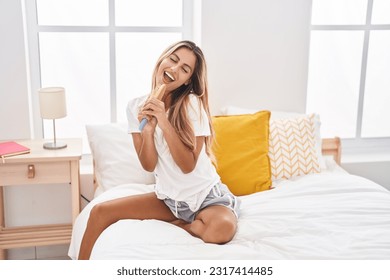 Young blonde woman singing song using brush as a microphone at bedroom - Powered by Shutterstock