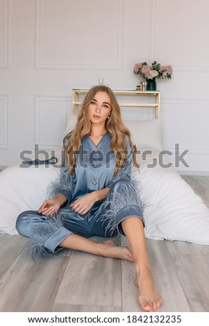 Young blonde woman sitting in blue pajamas on bed in white room