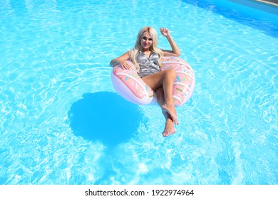 Young blonde woman sitting on a circle for swimming in a blue pool