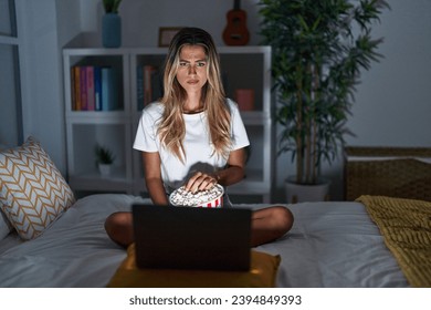 Young blonde woman sitting on the bed at home watching a movie from laptop skeptic and nervous, frowning upset because of problem. negative person. 