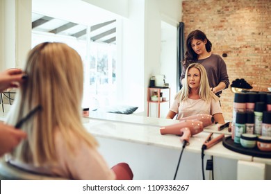 Young blonde woman sitting in a salon chair looking at her reflection in a mirror during an appointment with her hairstylist - Powered by Shutterstock