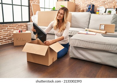 Young blonde woman smiling confident unboxing package at new home