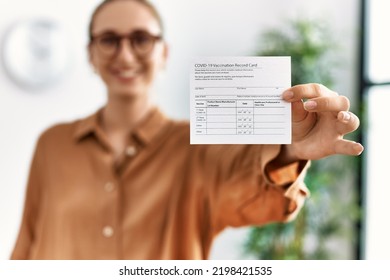 Young Blonde Woman Smiling Confident Holding Covid Vaccination Record Card At Waiting Room