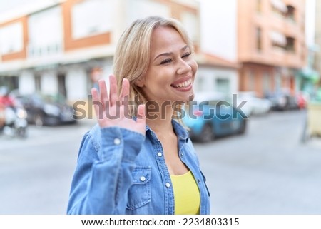 Young blonde woman smiling confident saying hello at street