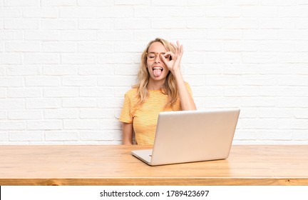 Young Blonde Woman Smiling Happily With Funny Face, Joking And Looking Through Peephole, Spying On Secrets Using A Laptop