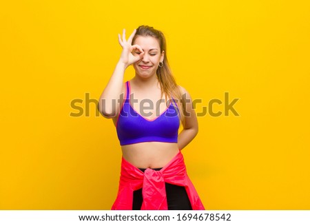 young blonde woman smiling happily with funny face, joking and looking through peephole, spying on secrets. sport concept