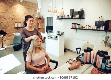 Young blonde woman smiling and looking at her reflection in a mirror while sitting in a salon chair during an appointment with her hairstylist