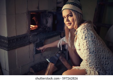 Young Blonde Woman Spliting Logs And Burning Wood In Stove At Home