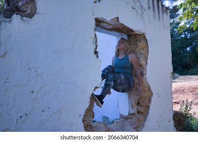 Young Blonde Woman In Sportswear, Doing Calisthenics Exercises In A Window Of A Dilapidated Building. Concept, Calisthenics, Fitness, Exercise, Curvy Girl.