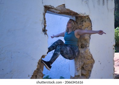 Young Blonde Woman In Sportswear, Doing Calisthenics Exercises In A Window Of A Dilapidated Building. Concept, Calisthenics, Fitness, Exercise, Curvy Girl.