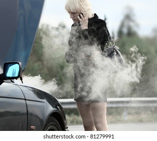 Young blonde woman standing by smoking and broken car and calling with cell phone