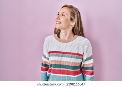 Young Blonde Woman Standing Over Pink Background Looking Away To Side With Smile On Face, Natural Expression. Laughing Confident. 