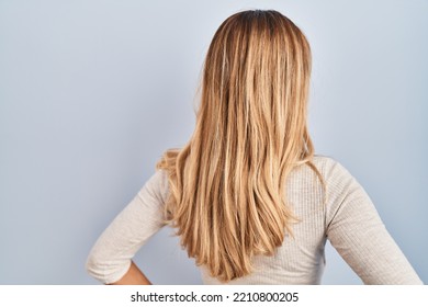 Young blonde woman standing over isolated background standing backwards looking away with arms on body  - Powered by Shutterstock