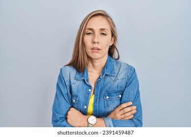 Young blonde woman standing over blue background looking sleepy and tired, exhausted for fatigue and hangover, lazy eyes in the morning. 