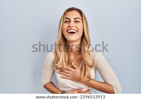 Young blonde woman standing over isolated background smiling and laughing hard out loud because funny crazy joke with hands on body. 