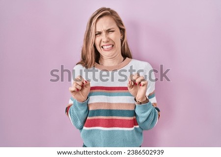 Young blonde woman standing over pink background disgusted expression, displeased and fearful doing disgust face because aversion reaction. 