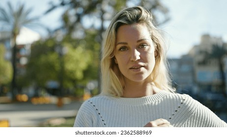 Young blonde woman standing with serious expression at park - Powered by Shutterstock