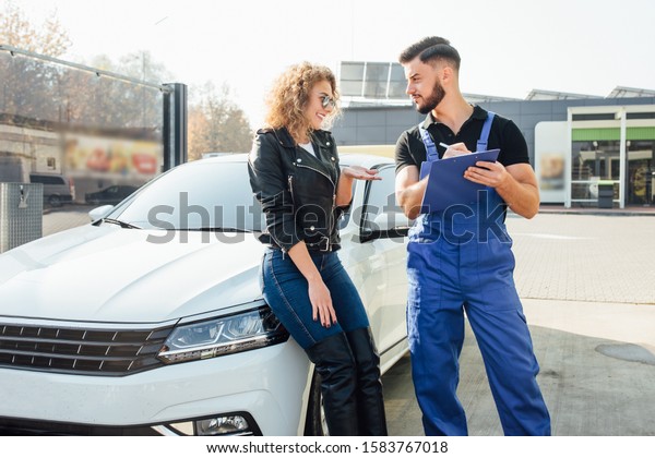 Young blonde woman stands\
with a man who washes cars at the self-service, give advices him\
about her car.