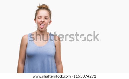 Young blonde woman sticking tongue out happy with funny expression. Emotion concept.