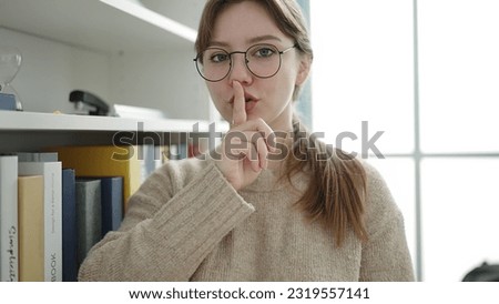 Young blonde woman student doing silence gesture at library university