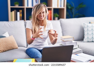 Young Blonde Woman Studying Using Computer Laptop At Home Shouting Frustrated With Rage, Hands Trying To Strangle, Yelling Mad 